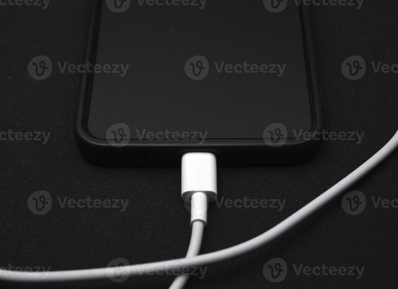 A mobile phone on a black background. A smartphone with a connection cable. photo