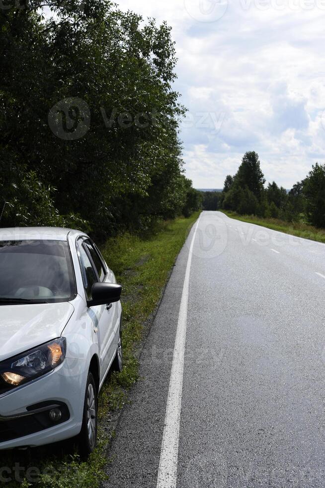 A white car by the expressway in the woods. Wet asphalt and a car. photo