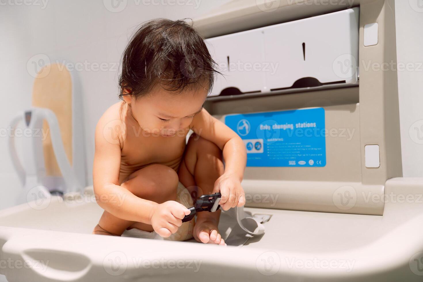 A boy is sitting at the Baby Changing Station waiting to be changed. The child is playing with the Belt Strap, it's prevent the child from falling out. photo
