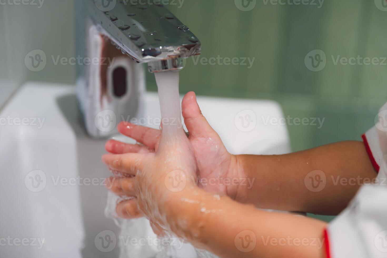 Washing Hands. A close-up shot of a child's hands diligently washing under running water in a bathroom sink. The image emphasizes the importance of hygiene and cleanliness, with a focus on the gentle photo