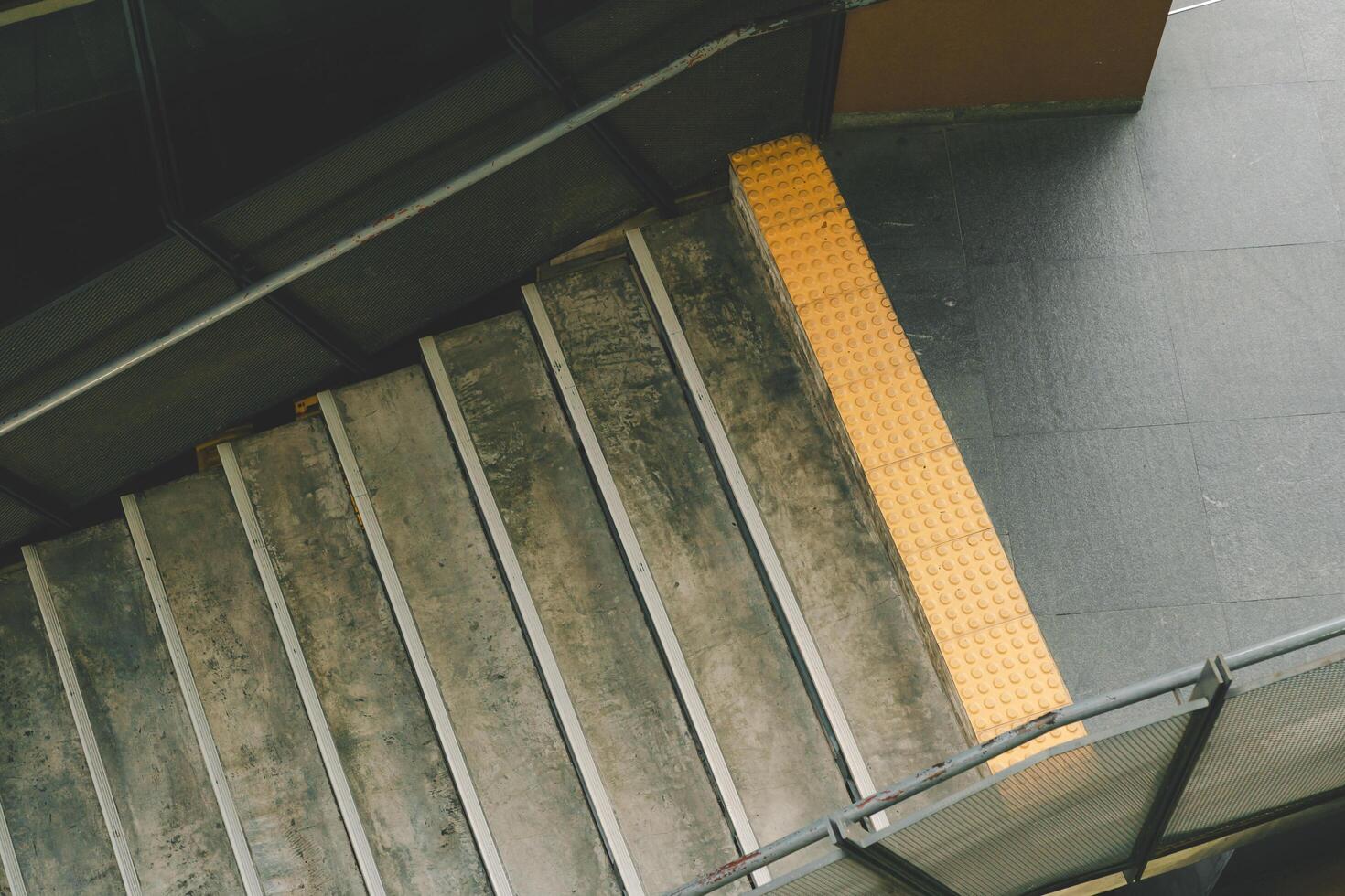 Stairs leading up to a higher level. The stairs are made of concrete and have a worn, weathered appearance. There is a yellow tactile warning strip on the side of the stairs. photo