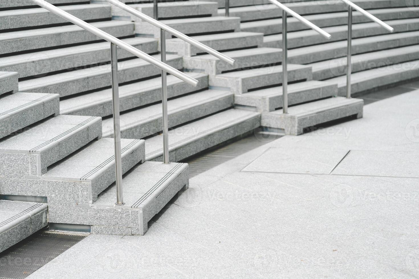 A modern staircase with wide, smooth concrete steps and sleek stainless steel handrails. The steps descend in a symmetrical pattern, creating a clean and minimalist aesthetic. photo