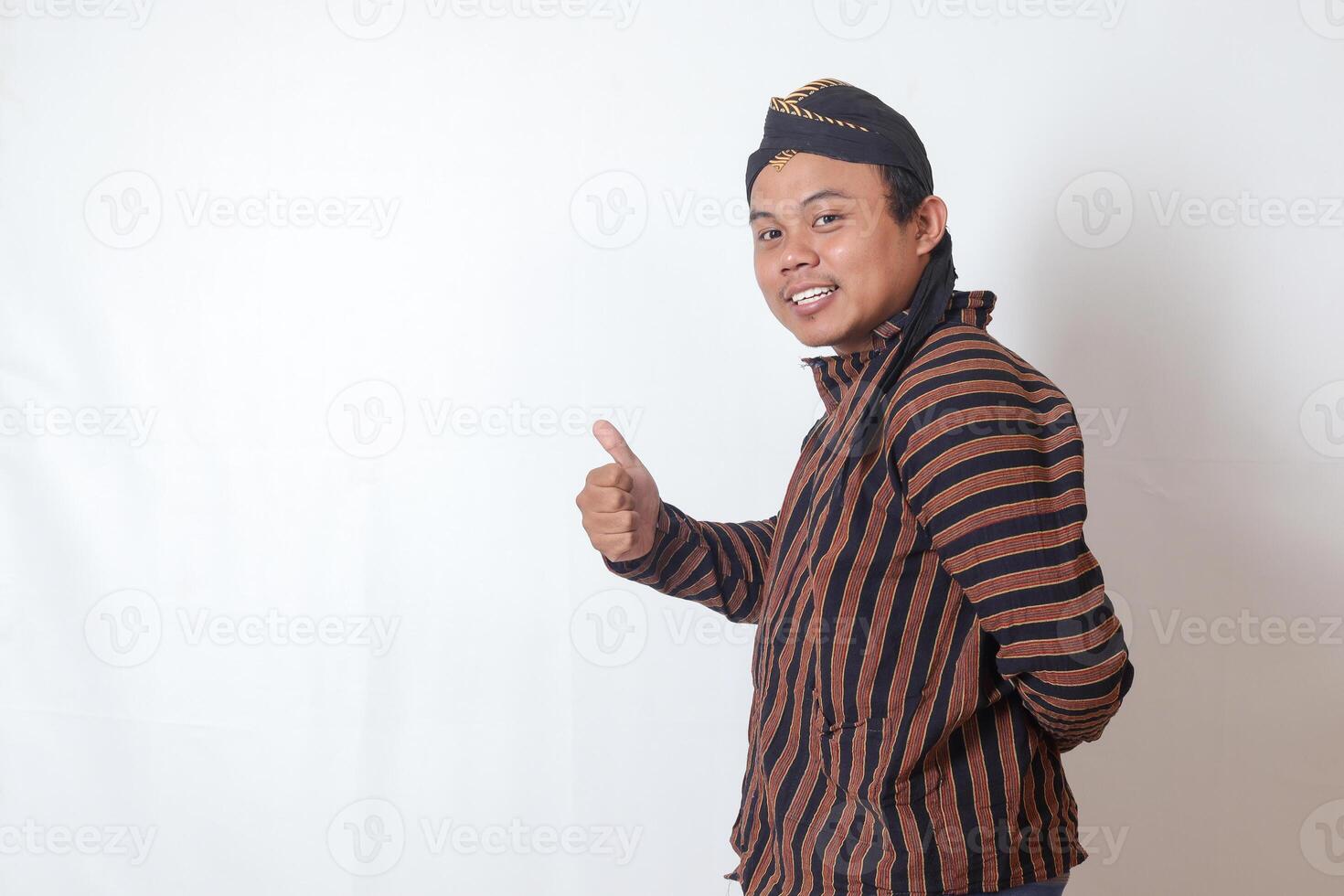 Portrait of friendly Asian man in javanese cloth with blangkon hat inviting someone to come in the most polite manner. Isolated image on white background photo