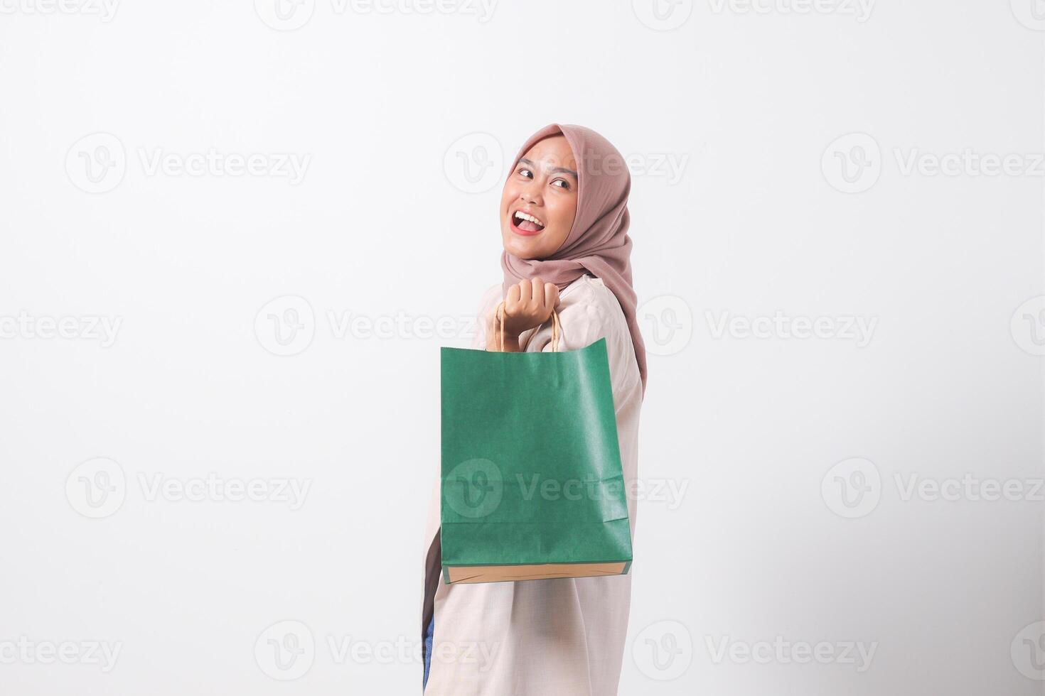 Portrait of cheerful Asian hijab woman in casual suit holding and showing colorful paper shopping bags. Shopaholic girl and discount buying concept. Isolated image on white background photo