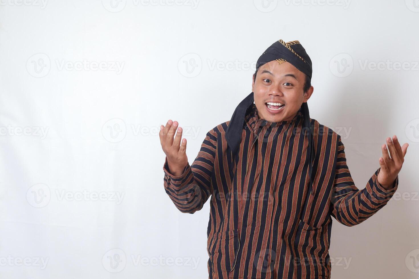 Portrait of excited Asian man in javanese cloth with blangkon hat pulling hands towards camera, inviting someone to come inside, welcoming gesture. Isolated image on white background photo