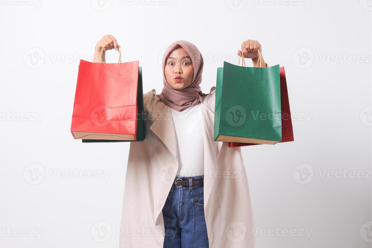 Portrait of attractive Asian hijab woman in casual suit holding and showing colorful paper shopping bags. Shopaholic girl and discount buying concept. Isolated image on white background photo
