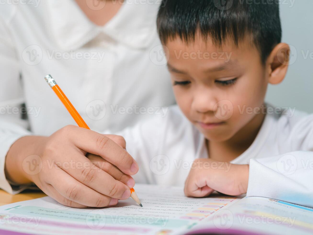Teacher or mother helping boy writing lesson and learning to write, Education home school concept, Female tutor helping little elementary school boy with homework during individual lesson at home photo