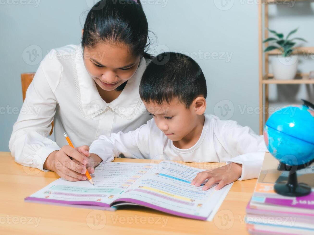 Female tutor helping little elementary school boy with homework during individual lesson at home, Teacher or mother helping boy writing lesson and learning to write, Education home school concept. photo