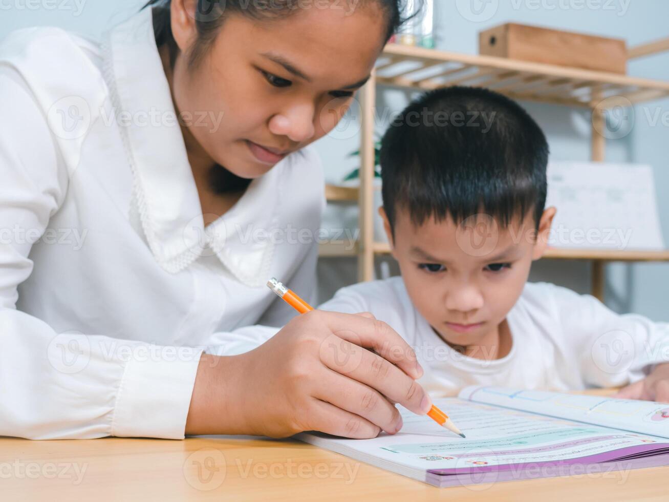 Teacher or mother helping boy writing lesson and learning to write, Education home school concept, Female tutor helping little elementary school boy with homework during individual lesson at home photo