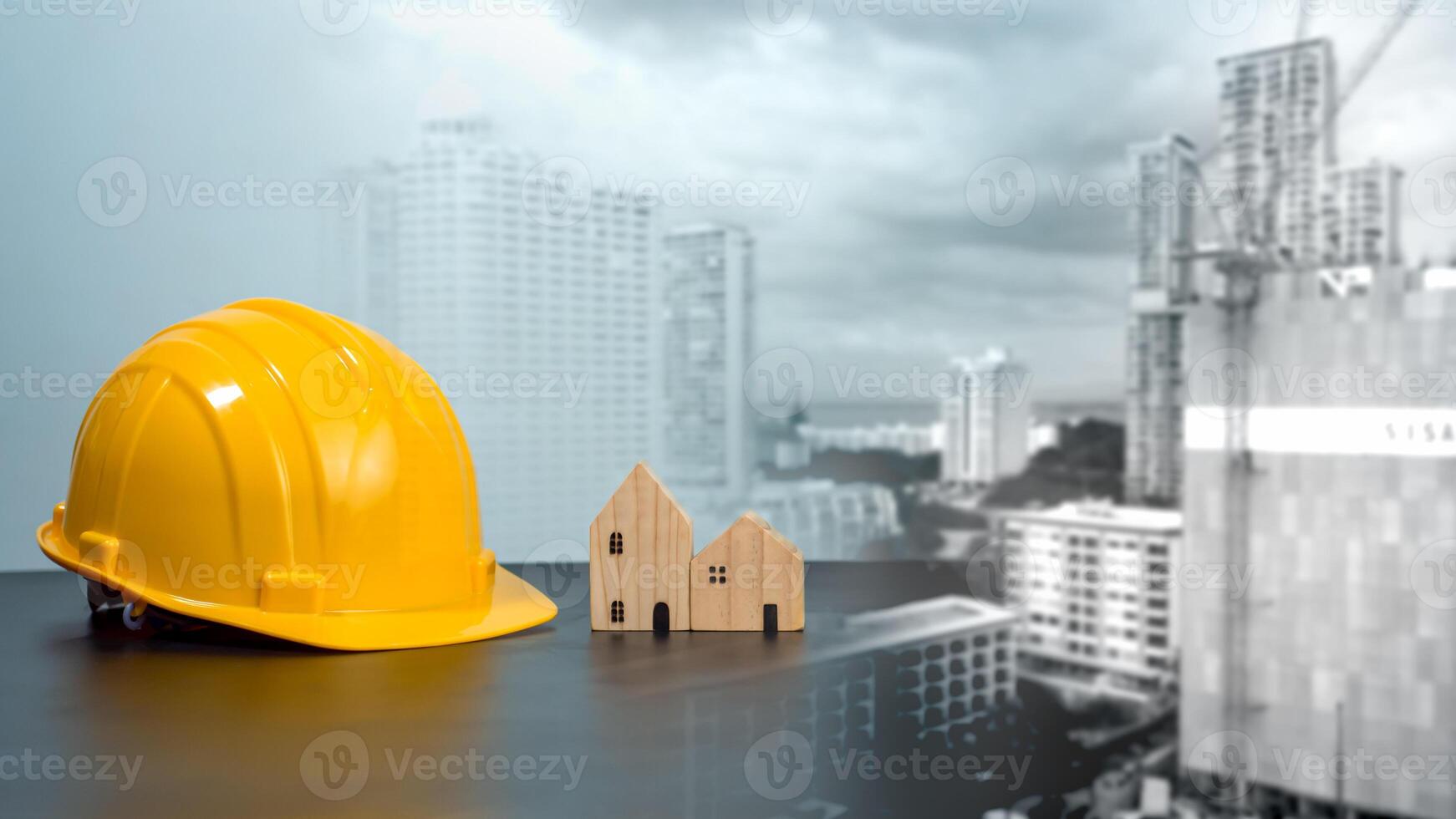 Hard hat and wooden house mockup placed at black tabletop on double exposure background of high building and construction site. Project planning presentation, project presentation and project design. photo