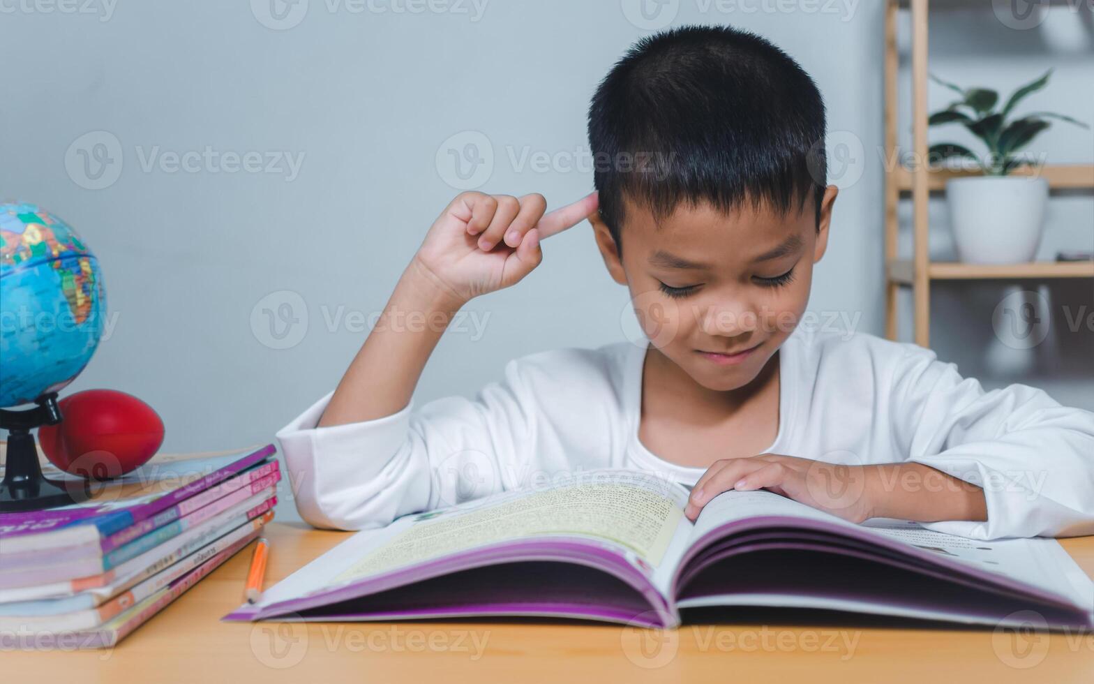 The child smile thinking sitting at table with book. Education, Childhood, People, Homework and school concept. Student learning study reading book while sitting at home. photo