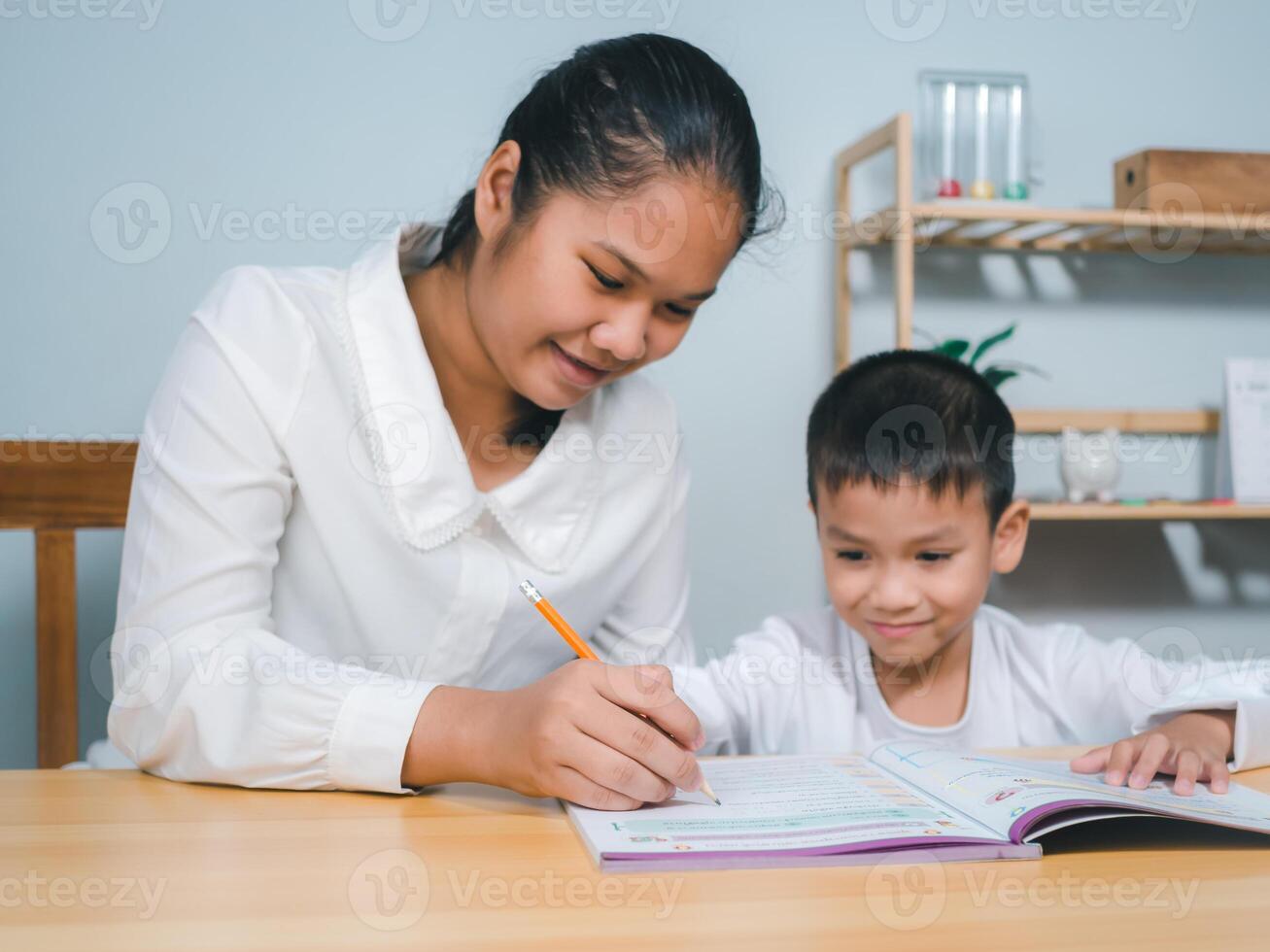 Female tutor helping little elementary school boy with homework during individual lesson at home, Teacher or mother helping boy writing lesson and learning to write, Education home school concept. photo