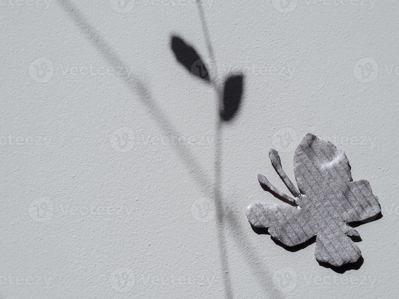 Silver painted cardboard butterfly on white wall and tree silhouette for copy space, nature and environment concept. photo