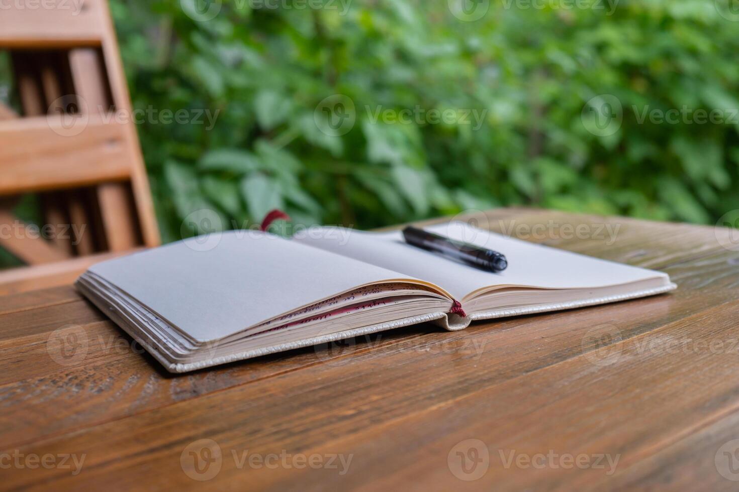 Empty white open paper notebook in wooden table outdoors in garden. Concept of self reflection discovery journal, writing gratitude journal photo