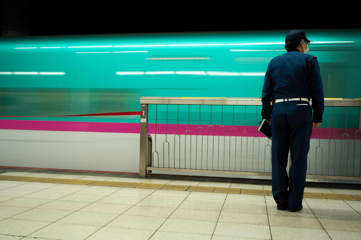 Back portrait of worker stands in the platform of the Shinkansen station with motion blurred train in background photo