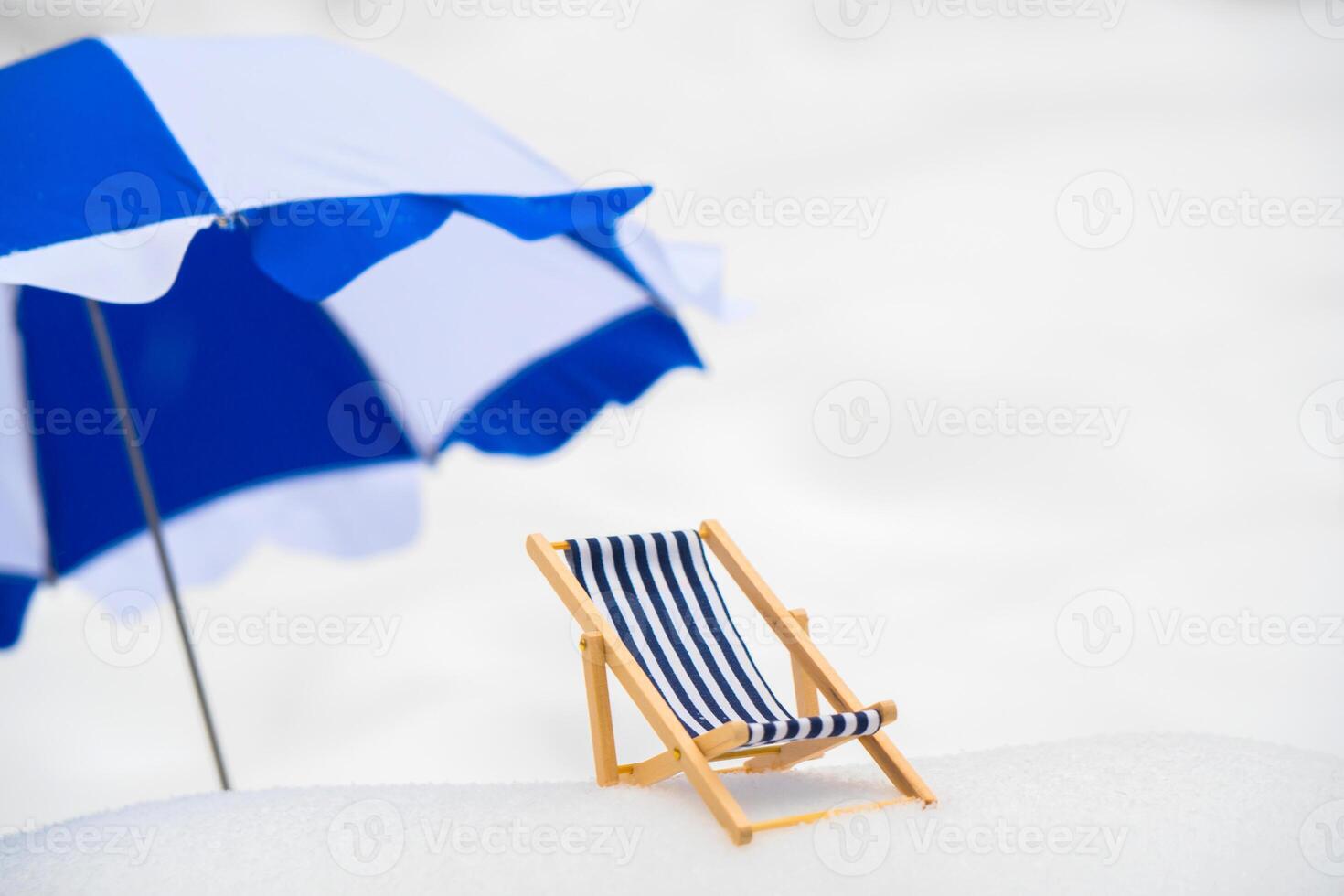A blue, wooden, striped wooden beach chair in the snow. photo