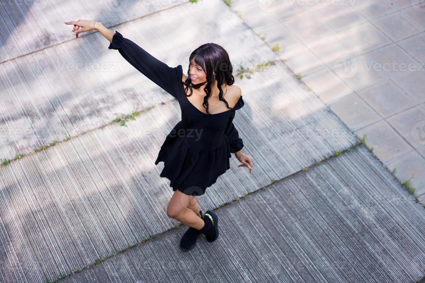 Energetic woman dancing a choreography wearing black summer dress outdoors photo