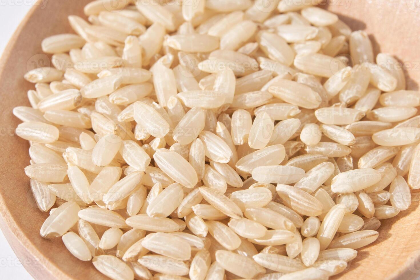 A closeup of long, uncooked brown rice grains on a wooden spoon surface, emphasizing the healthy, natural aspect of this whole food. Pile gluten texture photo