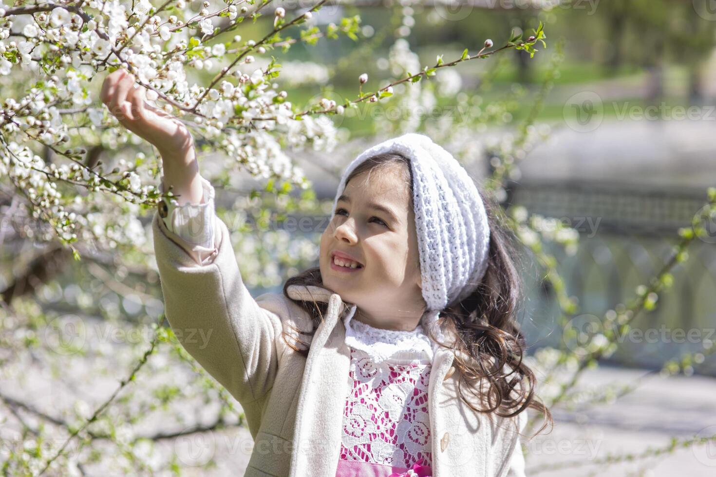 a little girl in a white coat, holding a branch of a tree blooming with white flowers photo