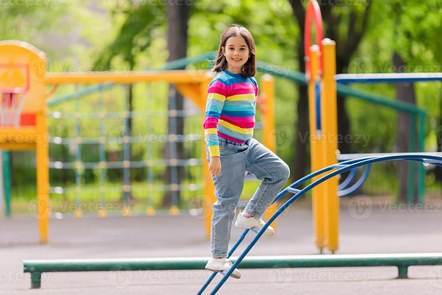 a girl in a bright striped jumper and jeans, stand on the childrens stairs on the playground photo