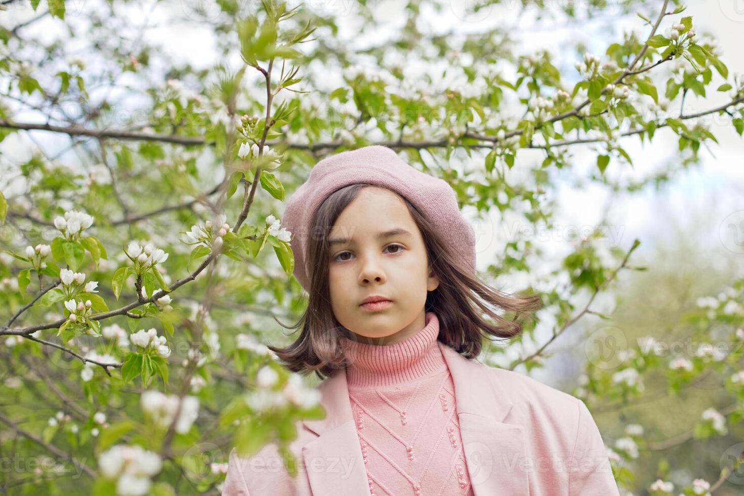 Portrait of beautiful little girl stands in a blooming white apple tree in the park. photo