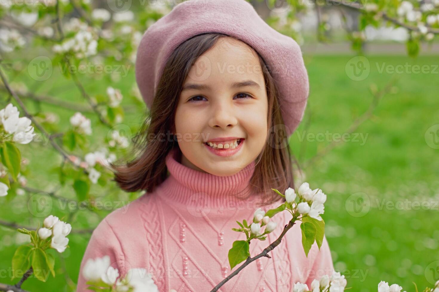 Portrait of happy little girl stands in a blooming white apple tree in the park. photo
