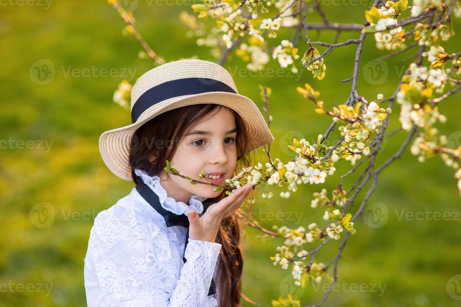 a beautiful girl in a white openwork dress, holding a branch of a tree blooming with white flowers photo