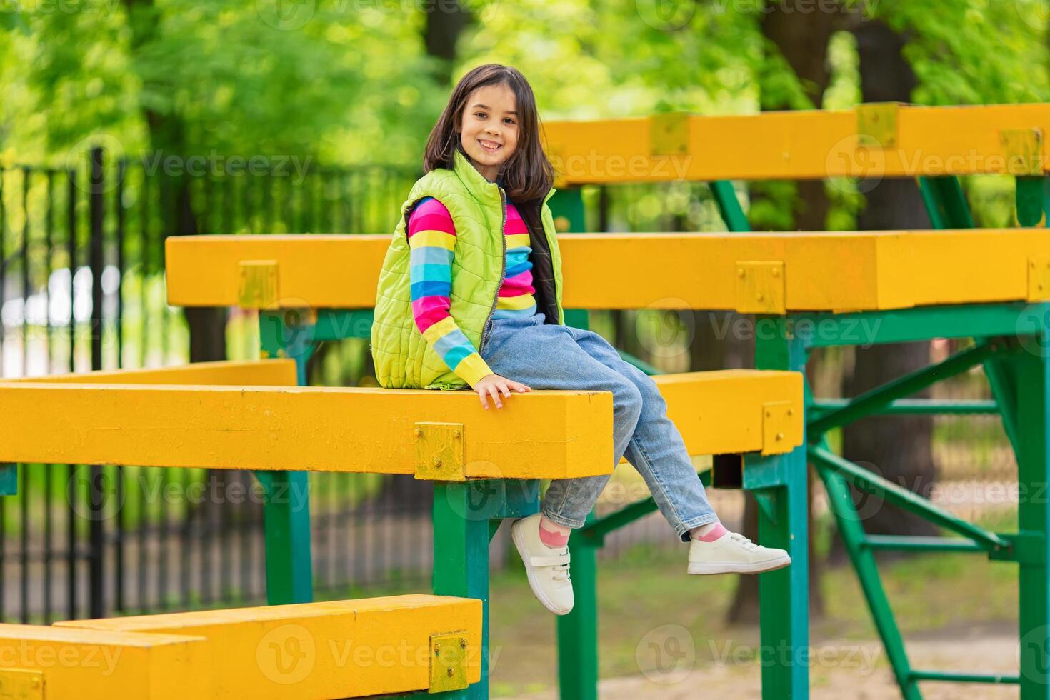 a cute smiling little girl, in a multi-colored striped jumper and a green vest photo