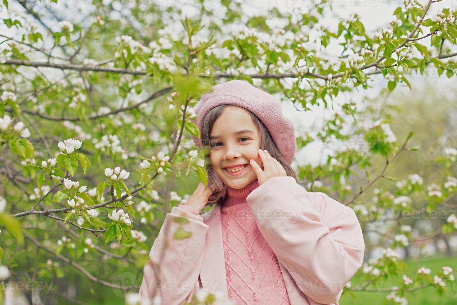 Portrait of a happy adorable little girl stands next to the branches of a blossoming white apple tree in the park. photo