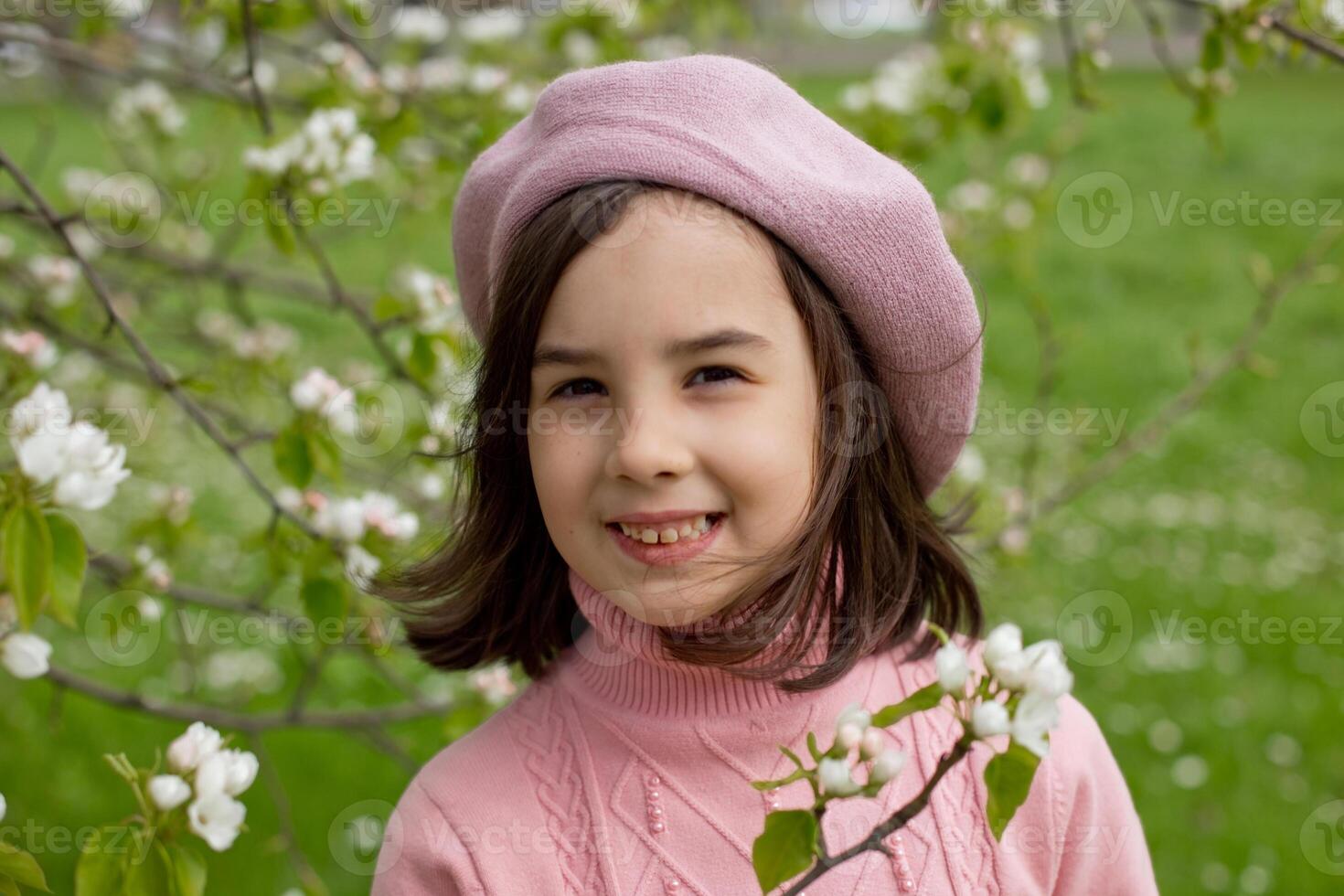 Portrait of beautiful happy little girl stands in a blooming white apple tree in the park. photo