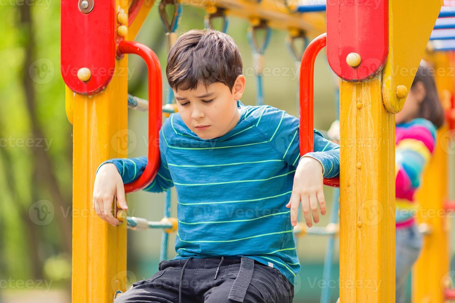 Sad and bored teen boy sitting on colorful playground in summer photo