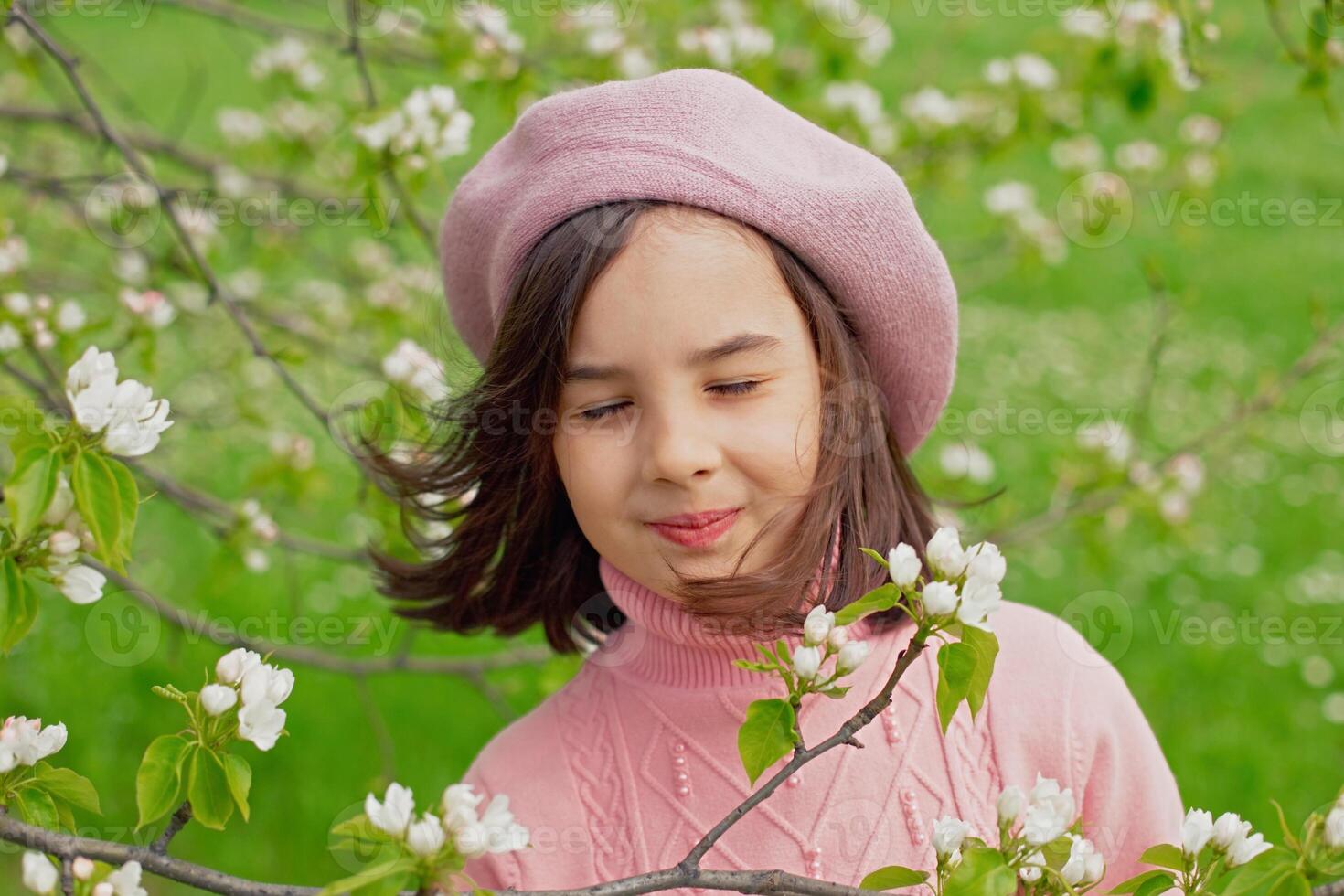 A happy little girl stands with her eyes closed in a blooming white apple tree in the park. photo