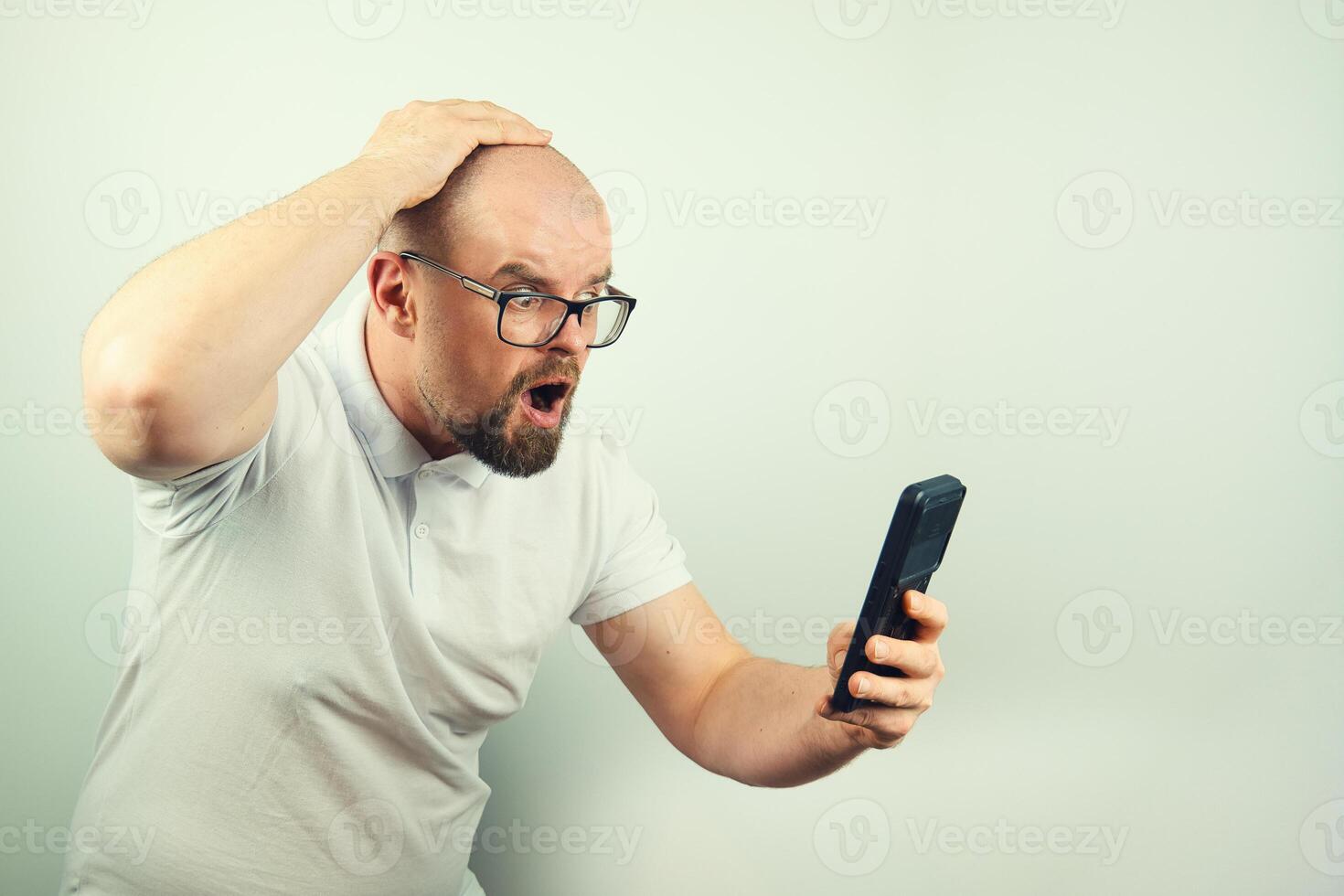 Portrait of surprised handsome bearded man with glasses and white shirt looking at mobile phone, facial expression, isolated on white background photo