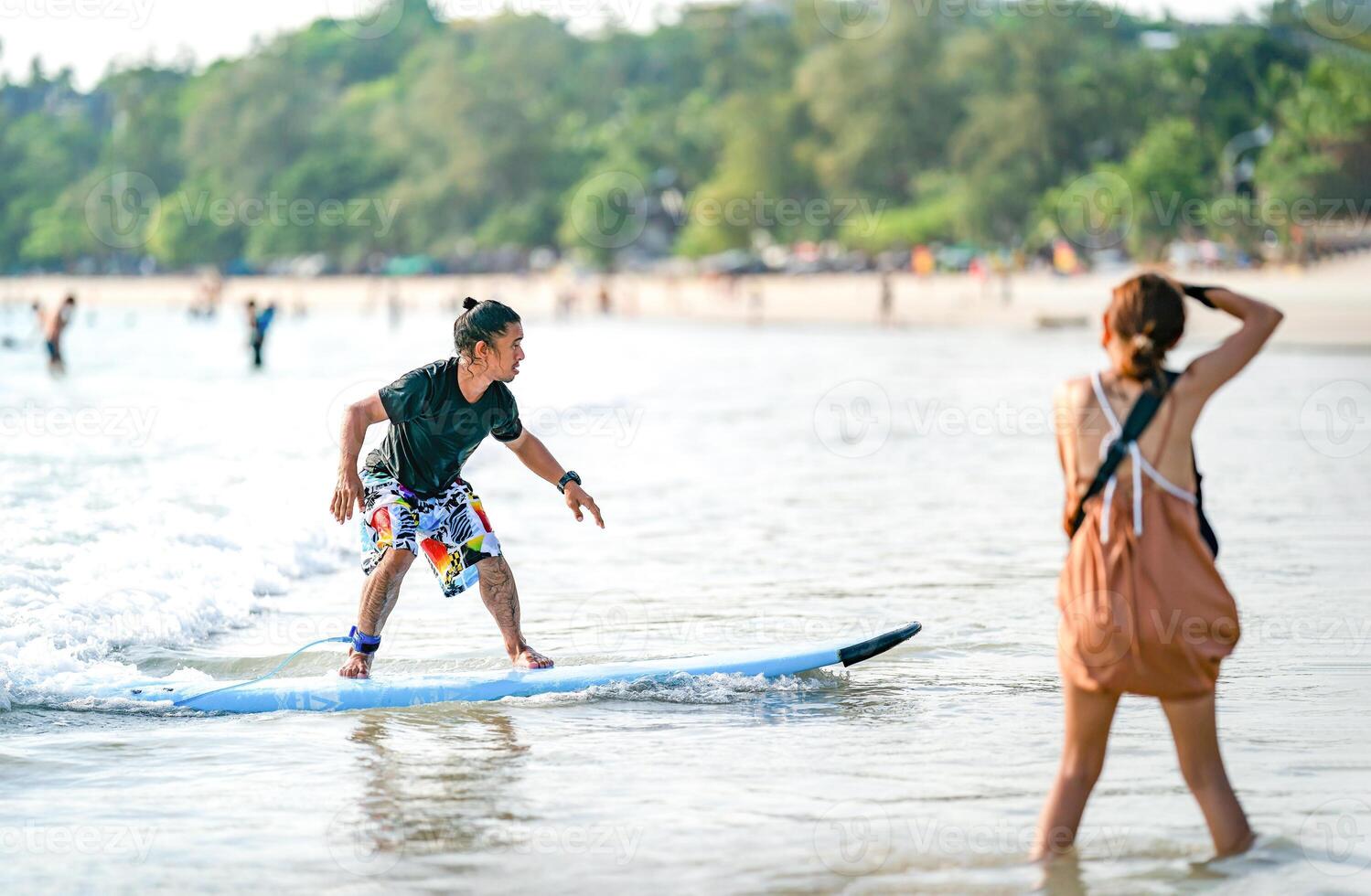 Amature surfman surfs the wave at Kata Beach, Phuket Province Thailand. While a blur woman is taking pictures at foreground beside him. photo