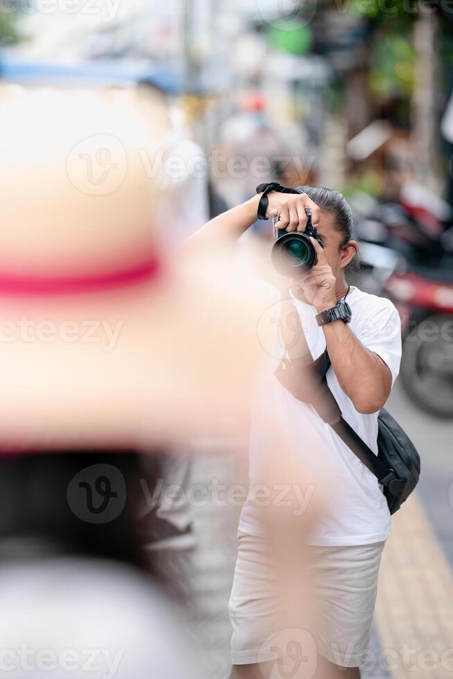 Professional Asian Camera man focus on the image with his mirrorless camera beside the street outdoor field. photo