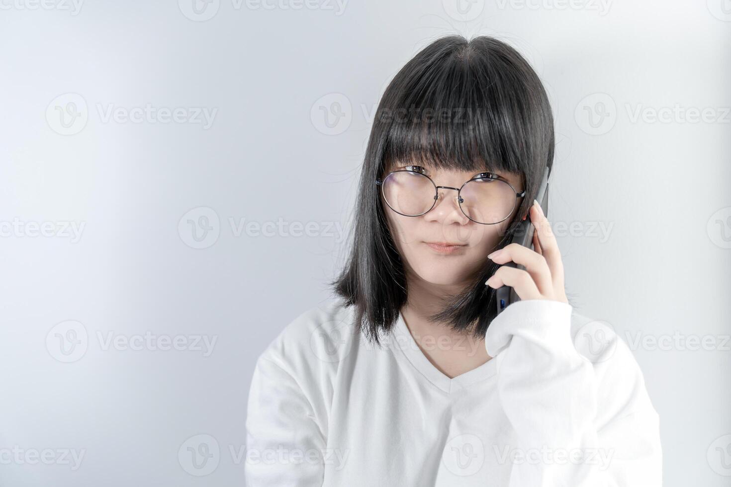 Isolated Pretty Asian glasses woman talks and speaks in the line with her mobile phone on white background in studio light. photo