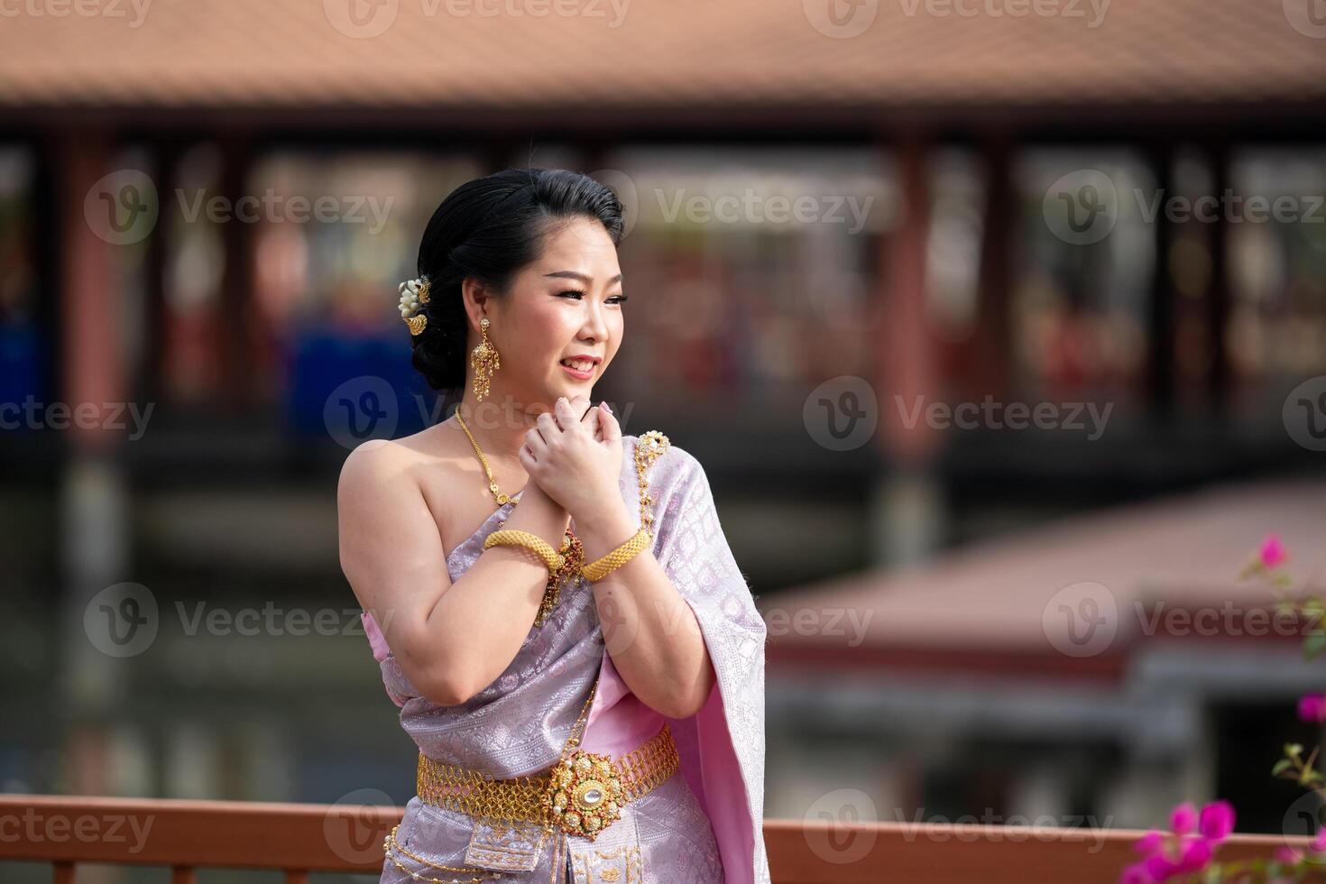 A woman in a traditional Thai costumes is standing on the wooden bridge while being taken a portrait photo shooting.