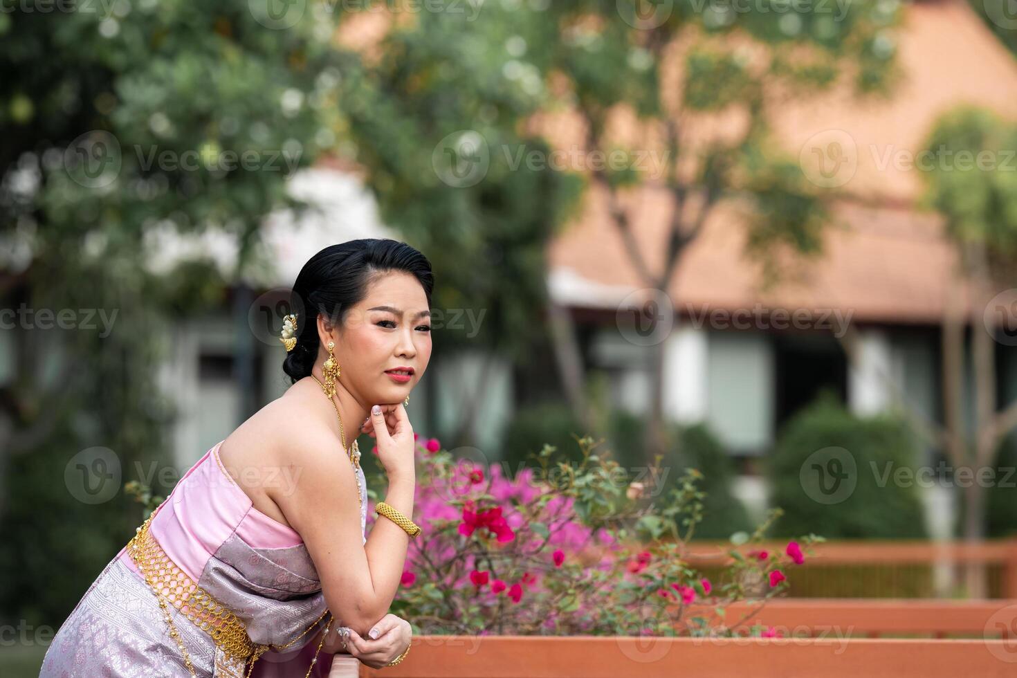 A woman in a traditional Thai costumes is standing on the wooden bridge while being taken a portrait photo shooting.