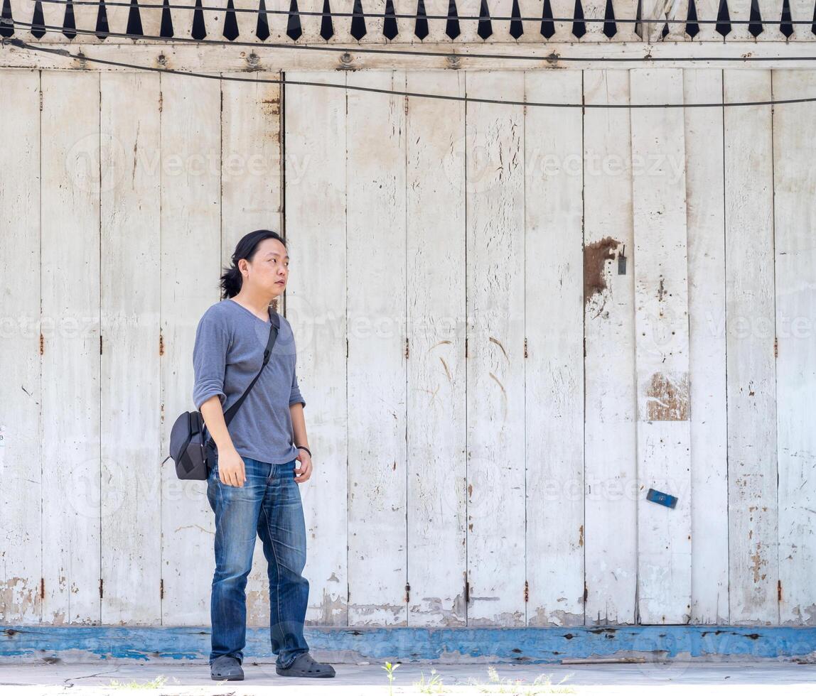 Asian long hair man is standing and posting in front of the Old white and blue wood wall on foot path of Asia vintage building for background. photo