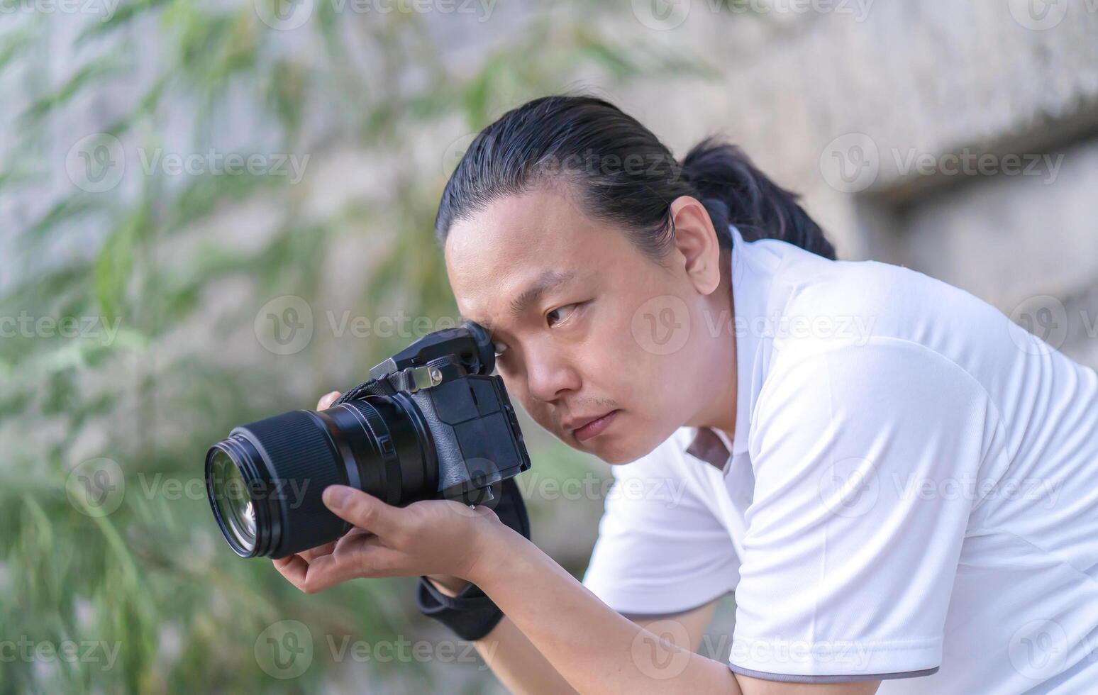 Professional Asian Chinese - Thai Camera man posture and focus in viewfinder and LED screen on mirrorless camera medium format in construction concrete area. photo