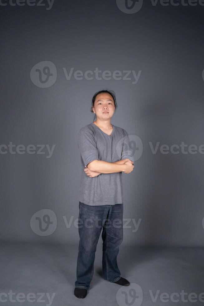Asian long hair friendly and positive man is posting and standing in front of gray background with studio light. photo