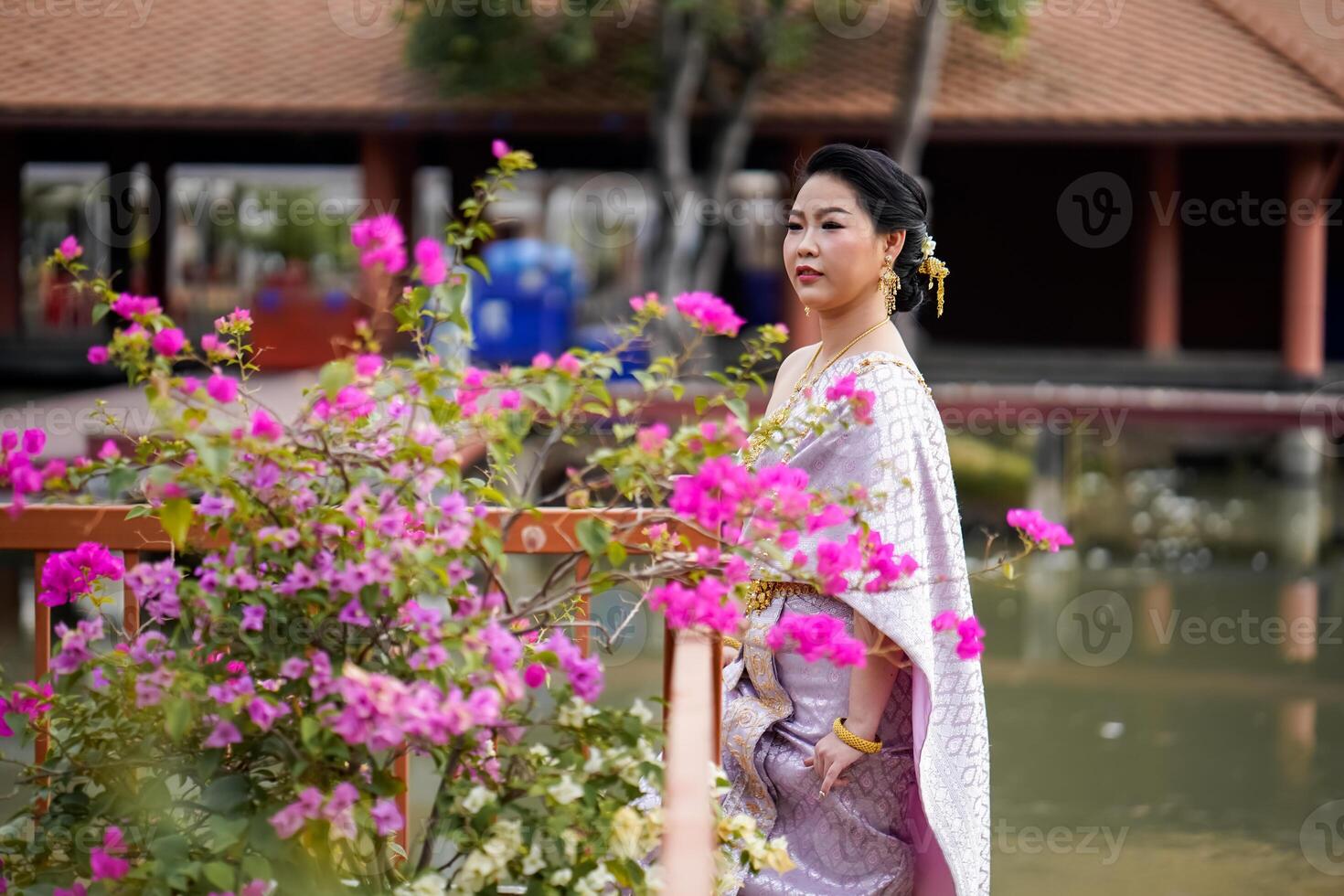 A woman in a traditional Thai costumes is standing on the wooden bridge while being taken a portrait photo shooting.