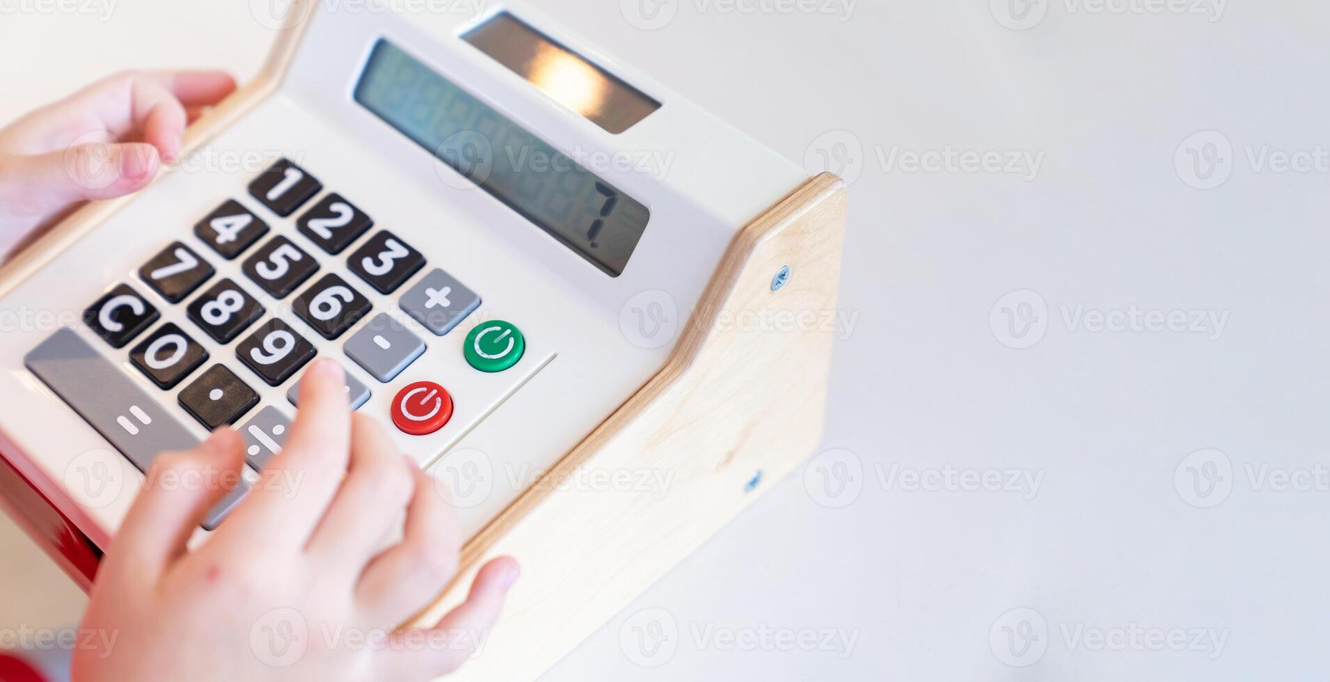 Kids are playing a wooden toy cash register by pressing the number seven, and others on it, respectively. photo