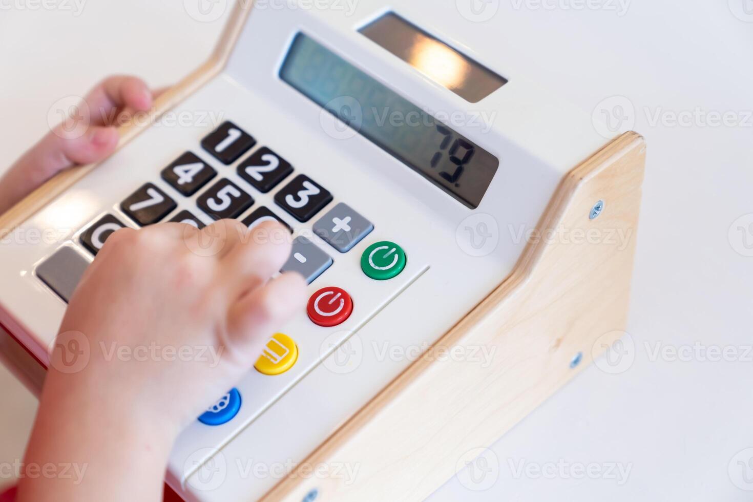 Kids are playing a wooden toy cash register by pressing the number seven, and others on it, respectively. photo