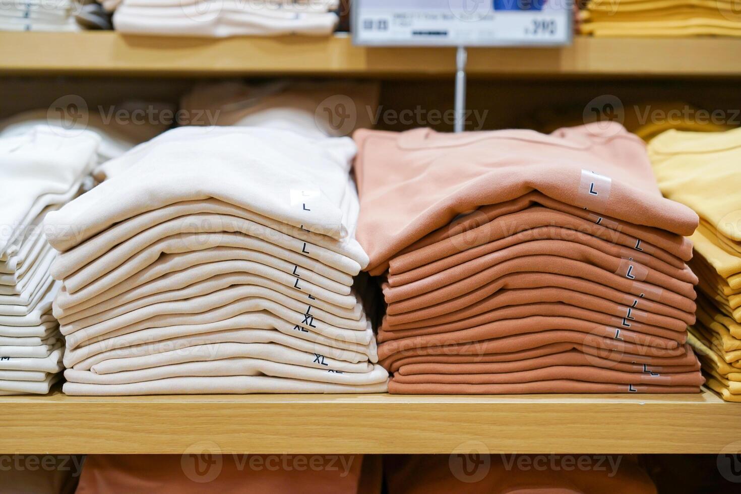 A pile of shirts, earth tone color, cream and brown was folded and put on shelf in cloth shop department store. photo