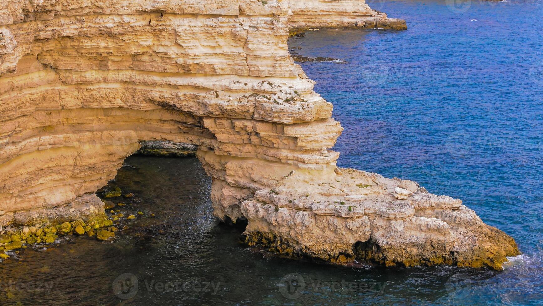 Steep rocky shore with an arch above the water with steppe vegetation, in eastern Crimea photo
