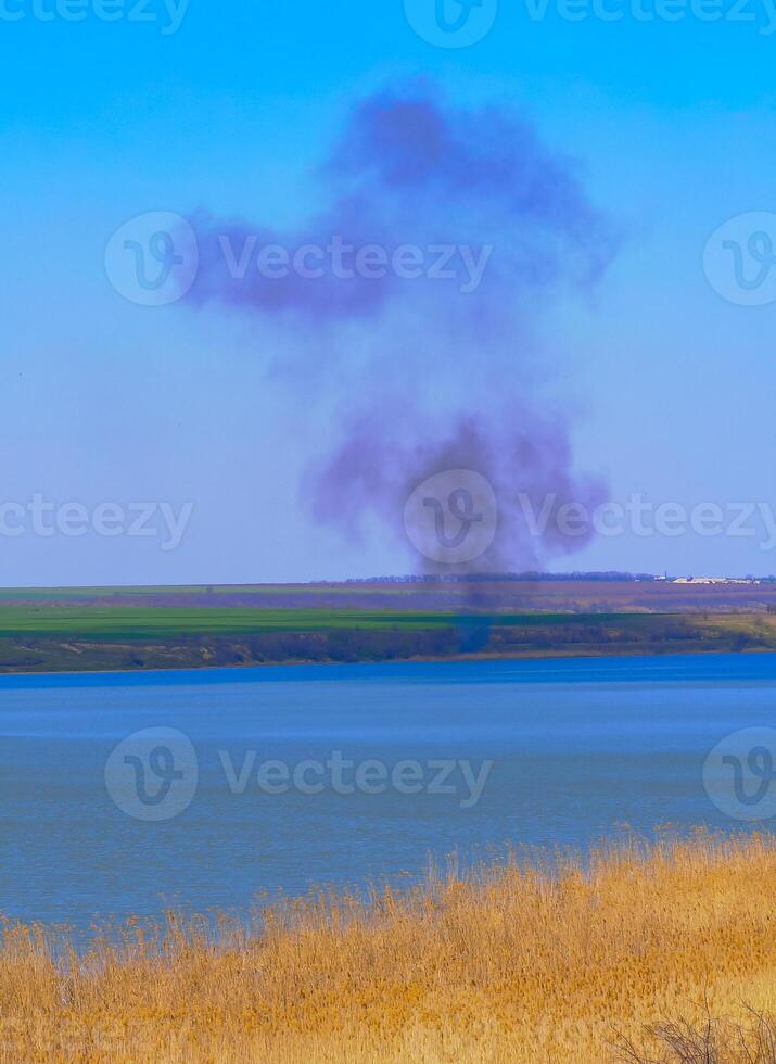 Fire at the lake shore, smoke from burning reeds in the background, Ukraine photo