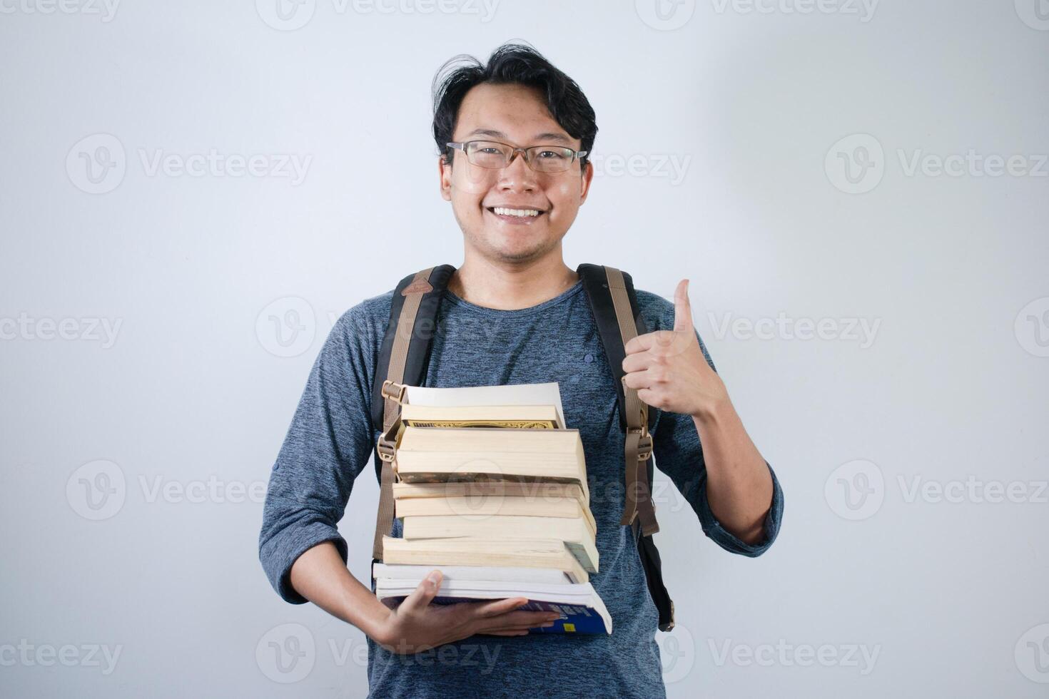 Asian young male student wearing bag and holding book smiling and happy expression. Ok hand sign gesture with isolated white background photo