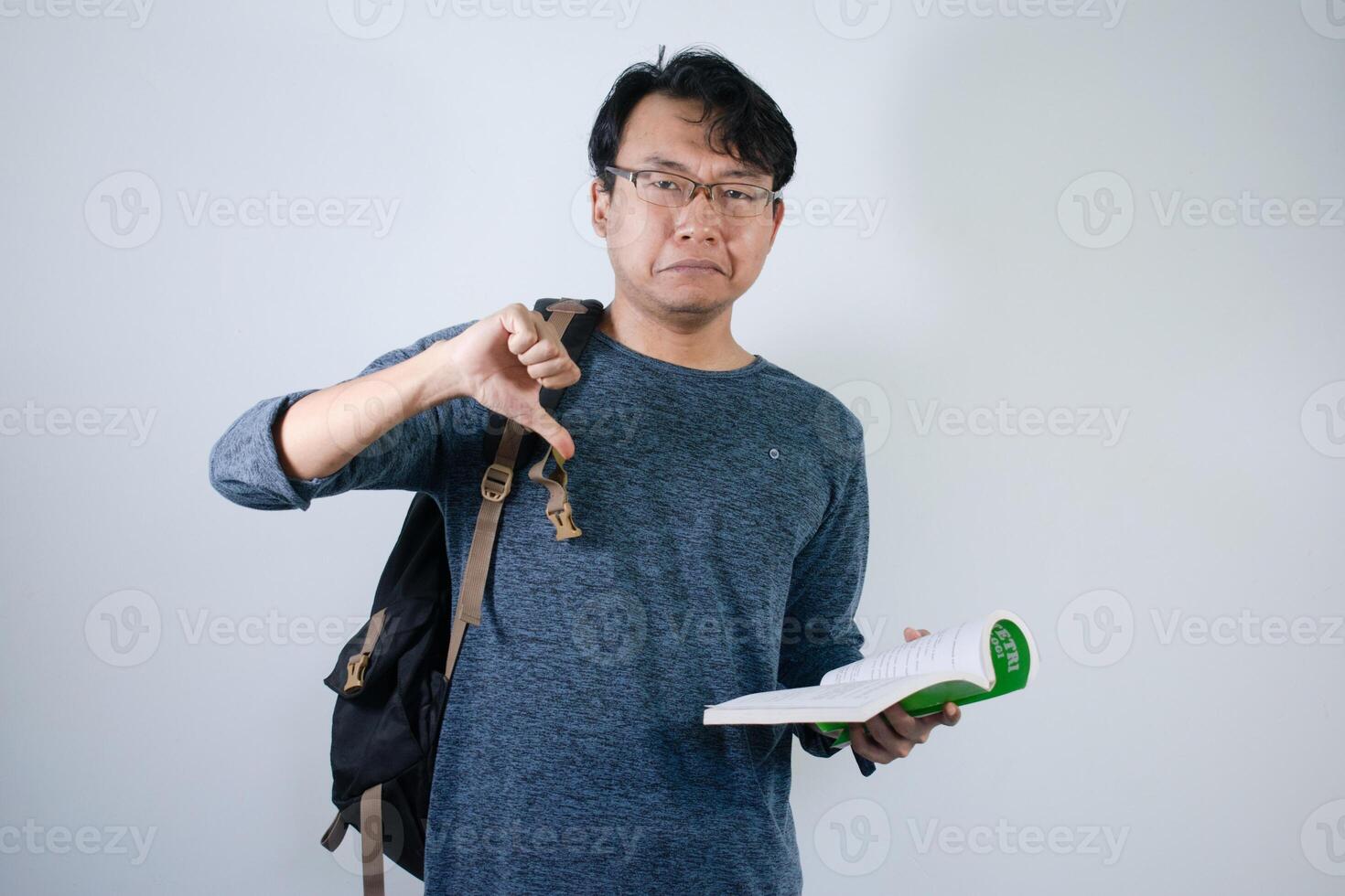 Asian young male reading book and making thumb down gesture. Male Student with glasses sad expression with Isolated white background photo