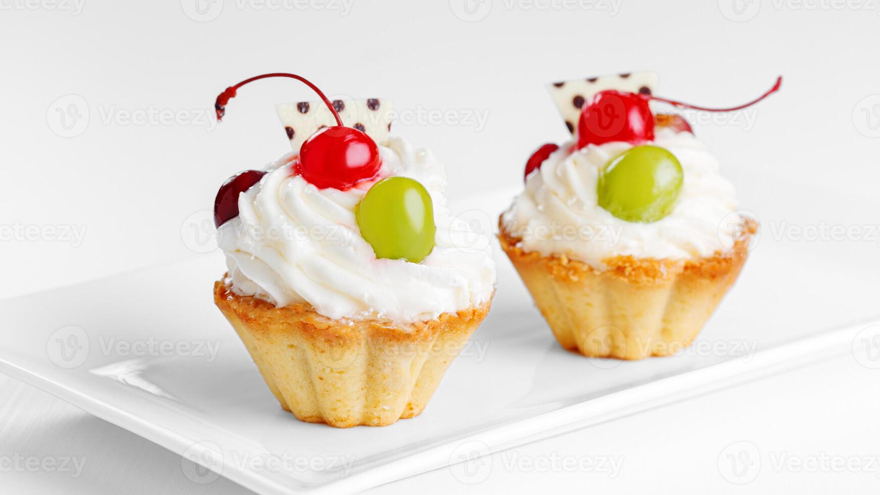 Beautiful cream cakes with cherries and grapes on a plate on a white background photo
